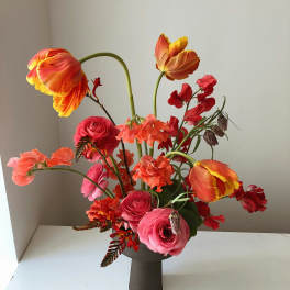 Bright mixed bouquet in a dark vase with orange tulips and pink ranunculus