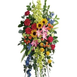 Tall standing spray of bright mixed flowers including roses, lilies, sunflowers, and delphinium on an easel