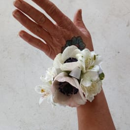 White floral wrist corsage with a pale pink bloom and small white flowers