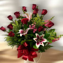 Tall arrangement of red roses and pink lilies in a white pitcher with a large red bow