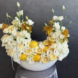 White and yellow floral arrangement in a white bowl with lemons and citrus slices
