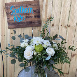 White roses and mums with a green accent bloom in a clear glass vase on a metal table.