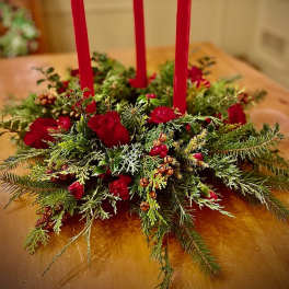 Low evergreen centerpiece with red roses and berries around three tall red taper candles