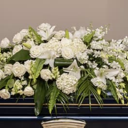 White casket spray of roses, lilies, and other white flowers on a dark casket