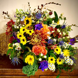 Colorful fall cornucopia arrangement with yellow sunflowers, orange roses, and mixed blooms in a woven horn basket