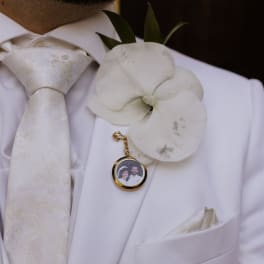 White orchid boutonniere on a white suit jacket with a photo charm