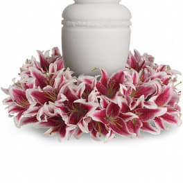 White cremation urn encircled by a wreath of pink and white lilies