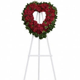 Heart-shaped wreath of red roses with ivy border on a tall white easel stand
