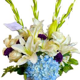 White lilies, cream roses, purple carnations, and blue hydrangea in a glass vase