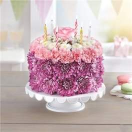 Pink and purple flower cake with striped candles on a white pedestal