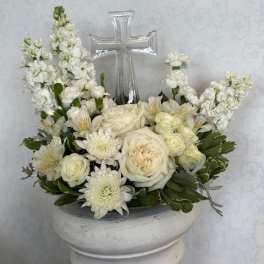 White floral arrangement with a clear cross centerpiece in a white pedestal vase