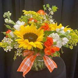 Bouquet of sunflowers, orange roses, and white flowers in a glass vase