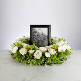 Round wreath of white roses and green orchids encircling a framed black-and-white photo