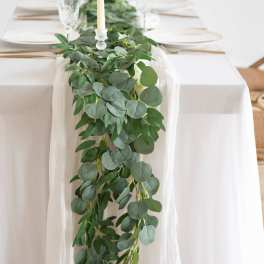 White table with a long eucalyptus greenery garland and tall ivory taper candles.