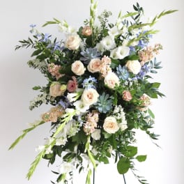 Tall standing spray of white, peach, and blue flowers arranged on a metal easel.