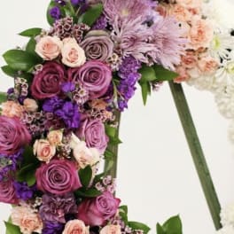 Standing wreath of pink and purple roses, carnations, and mums on an easel.