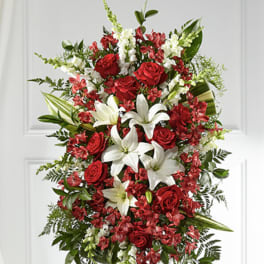 Standing spray of red roses, white lilies, and mixed red and white flowers on an easel.