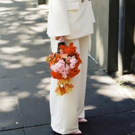 Person in white suit holding a colorful bouquet of pink and orange flowers