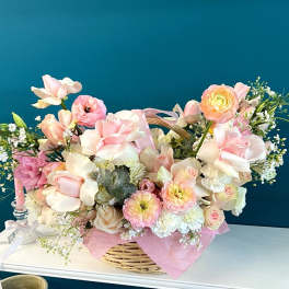 Pastel flower arrangement in a wicker basket with pink and cream blooms