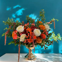 Mixed orange and white floral arrangement in a gold vase
