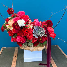 Bright red and pink floral arrangement with roses and a succulent in a white box