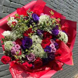 Large bouquet of red, purple, and pink flowers wrapped in red paper