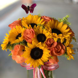 Sunflower and orange rose bouquet in a glass vase with pink ribbon