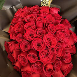 Bouquet of red roses wrapped in dark paper with a gold butterfly pick