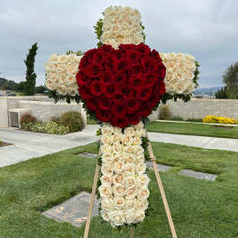 Large cross-shaped floral tribute made of red and white roses on an easel.