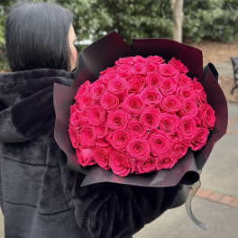 Person holding a large bouquet of bright pink roses wrapped in black paper