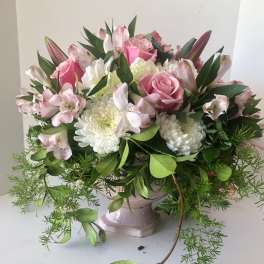 Pink roses and white blooms arranged in a pale pedestal vase
