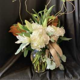 White floral arrangement in a glass vase with curly branches and a ribbon