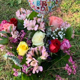 Birthday balloon above a colorful rose bouquet on grass