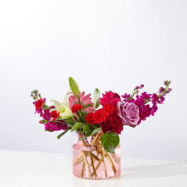 Mixed bouquet of pink, red, and white flowers in a pink glass vase
