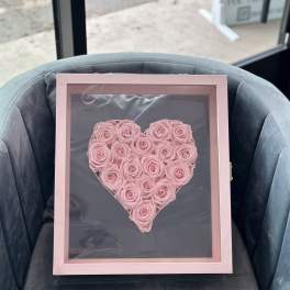 Pink roses arranged in a heart-shaped display inside a pink frame