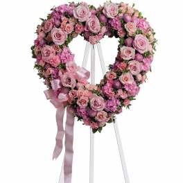 Heart-shaped pink floral wreath on a white stand with ribbon