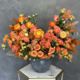 Orange and coral roses in a gray vase with autumn leaves