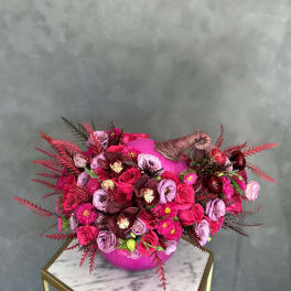 Pink and burgundy floral arrangement in a round vase with a wrapped handle