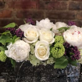 White roses and peonies with green and purple accents in a low arrangement
