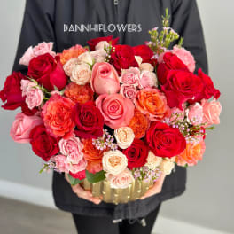 Large bouquet of red, pink, and peach roses in a gold container