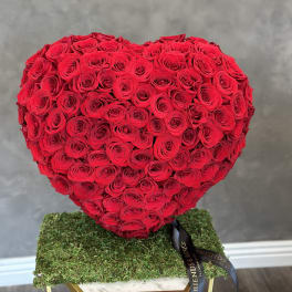 Heart-shaped arrangement of red roses on a moss-covered base