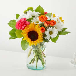 Mixed bouquet with a sunflower, daisies, roses, and carnations in a glass vase