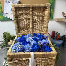 Blue roses and hydrangeas arranged in a woven basket with a white ribbon