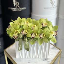 Green orchid arrangement in a white rectangular vase with ribbon