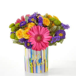 Colorful bouquet of gerbera daisies, roses, and purple blooms in a striped vase
