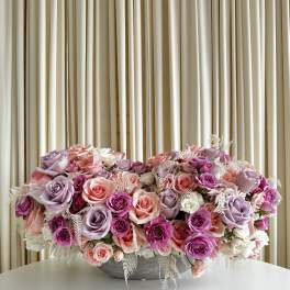 Low centerpiece of pink, lavender, and white roses in a gray bowl on a white table