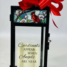Black lantern with a red bow and a candle reading Cardinals appear when angels are near