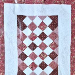 Patchwork quilt with a diamond pattern in pink, red, and white