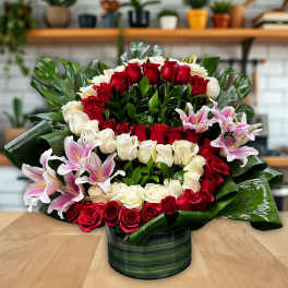 Red and white rose arrangement with pink lilies in a green vase