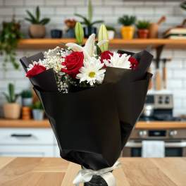 Bouquet of red roses, white lilies, and daisies in black wrap with a white ribbon
